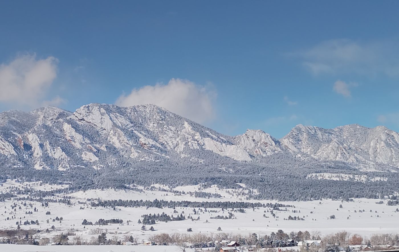 Snow-dusted Flatirons rising above a white valley beneath a deep blue winter sky